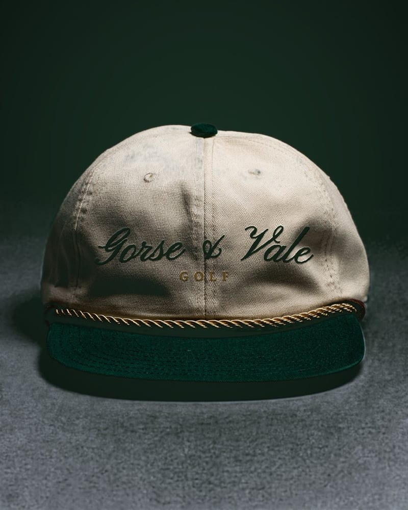 The Debut Cap — ivory cotton-twill crown, bottle-green brim, braided gold rope, and a leather strap.